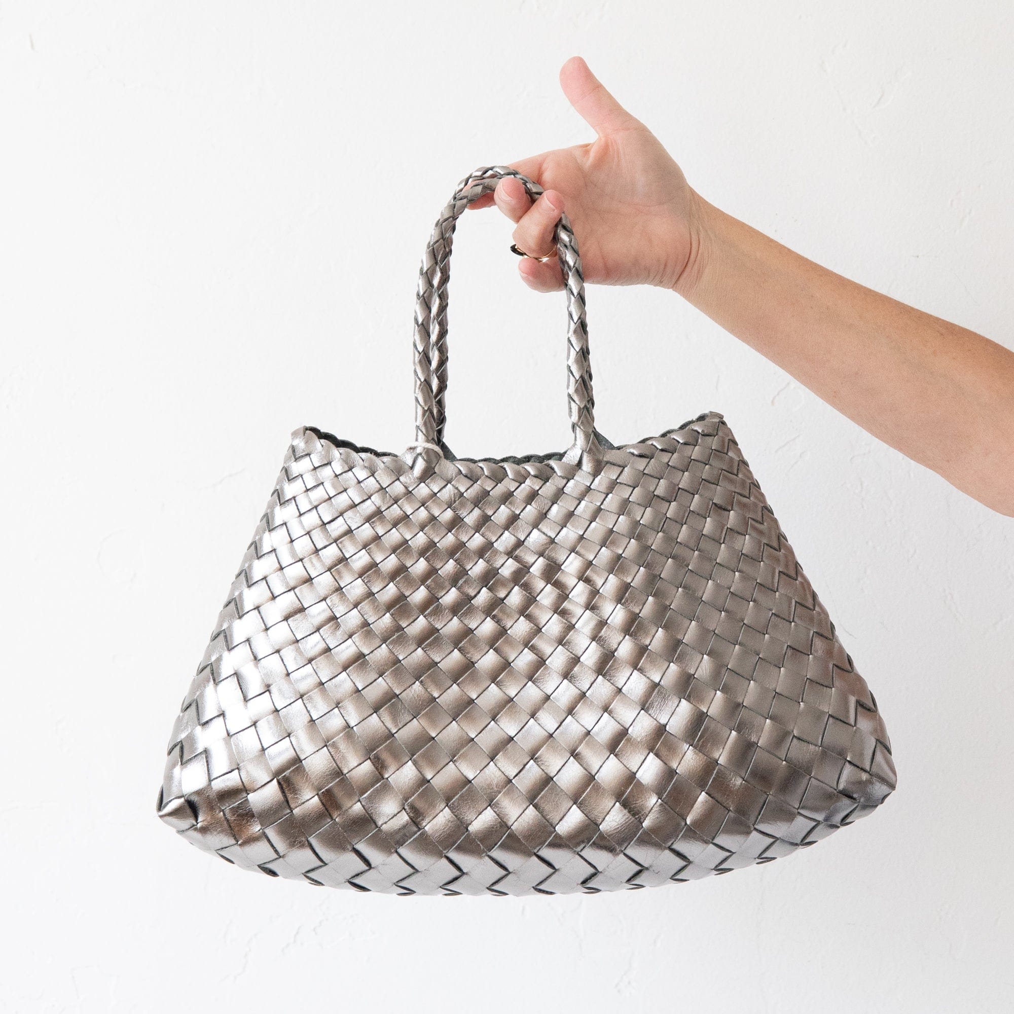 Hand holding a woven metallic bag against a white background