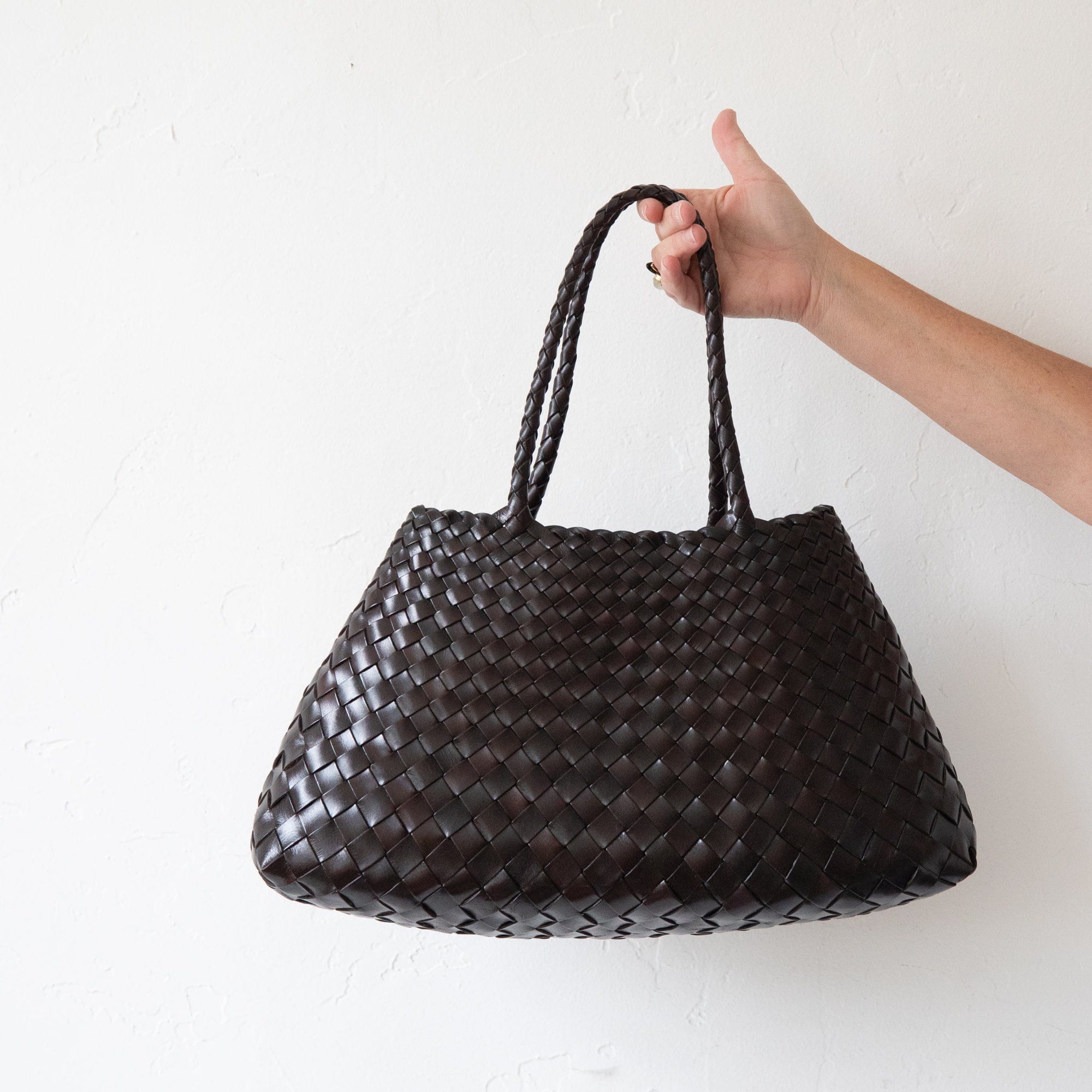 Hand holding a woven brown leather bag against a white background
